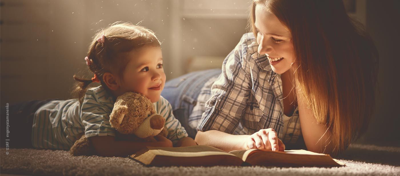 Babysitter, Foto: eine Frau und ein kleines Mädchen liegen auf dem Boden, liest Buch vor